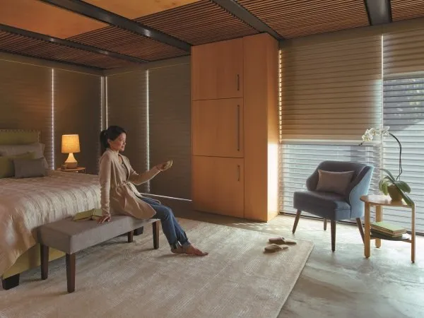 Woman operating motorized window shades in bedroom